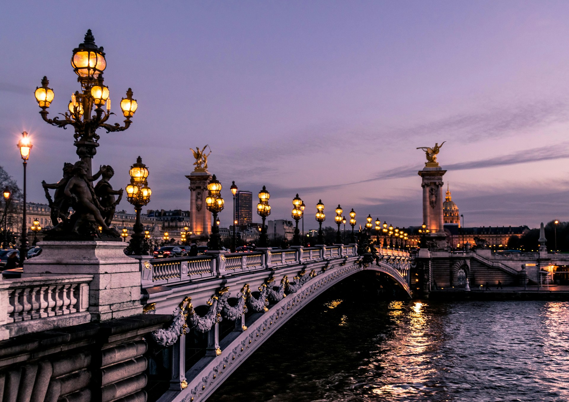 Parisian bridge lit by street lamps at night, with golden reflections shimmering on the Seine River.