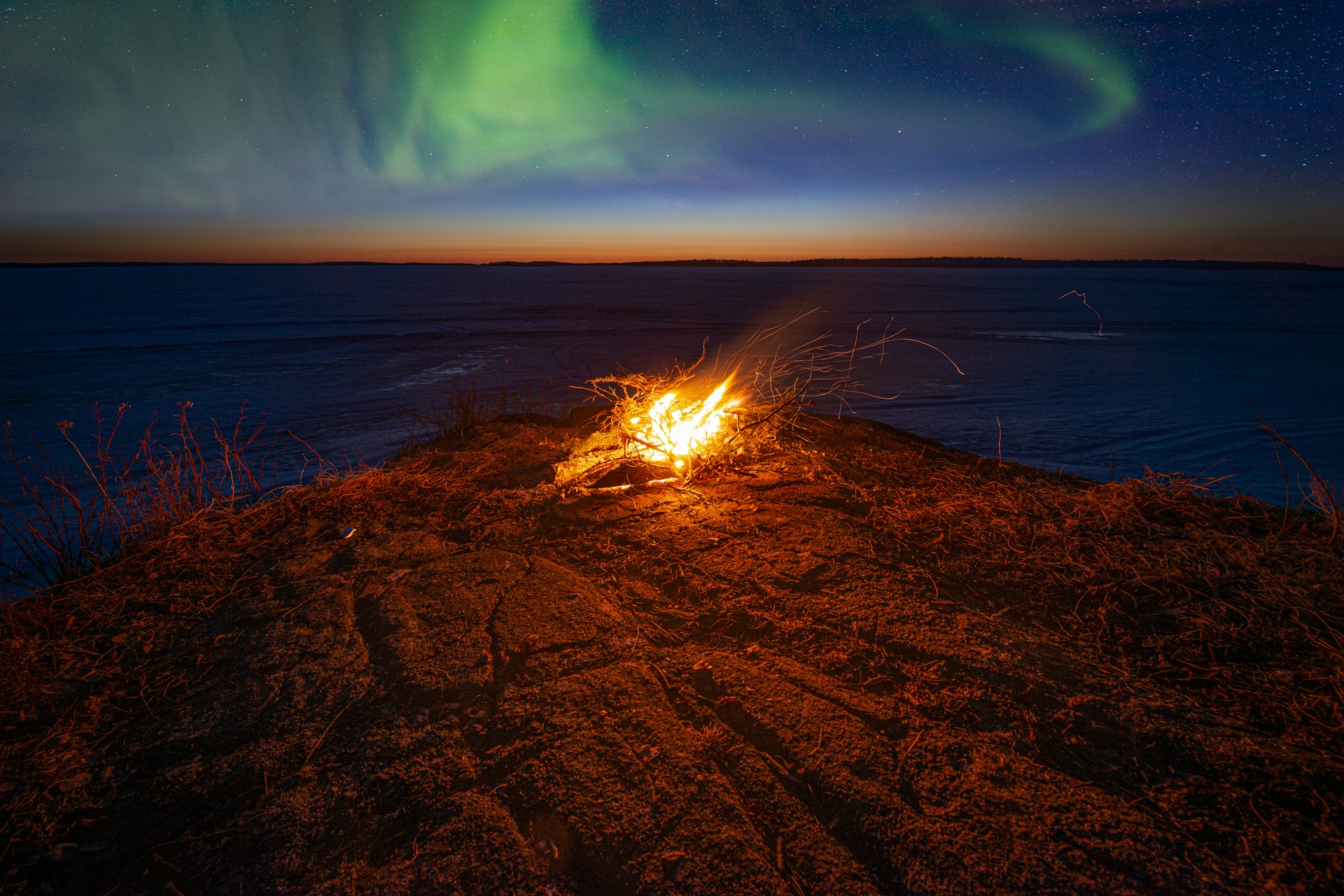 Vivid green and purple aurora borealis dancing across the night sky above the calm waters of Pinehouse Lake in Saskatchewan, Canada