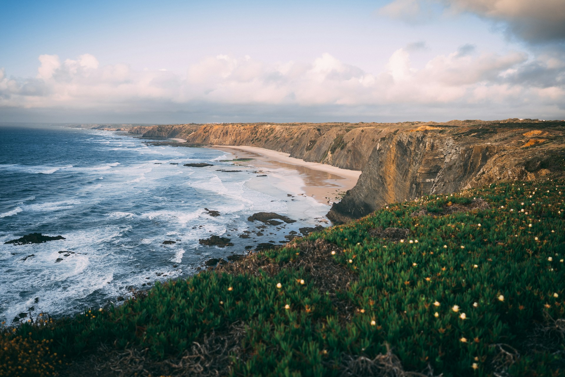 Scenic view of Aljezur, Portugal in spring, with lush green hills, blooming wildflowers, and whitewashed houses nestled in the valley.