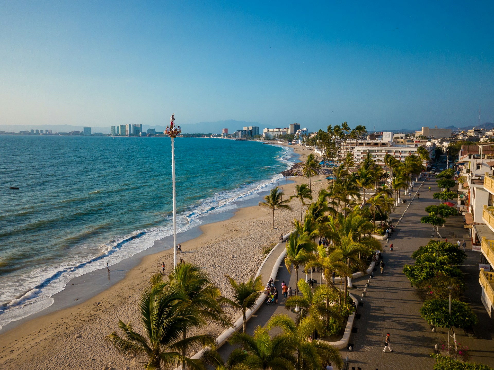 A sunny day on the beach in Puerto Vallarta with golden sand, gentle waves, and palm trees lining the shore.