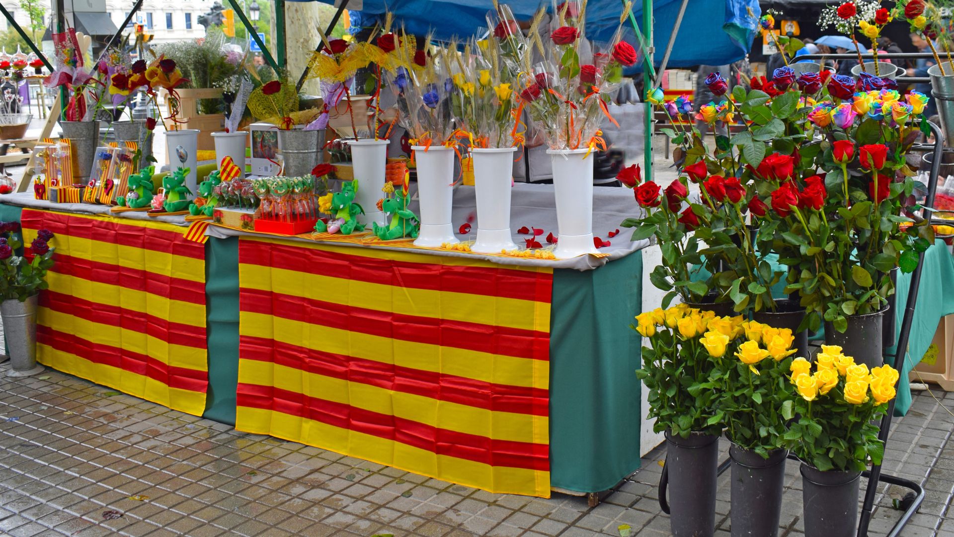 A street stall adorned with red and yellow striped fabric, showcasing bouquets of roses and other floral arrangements for sale, characteristic of the Sant Jordi festival in Catalonia, Spain. 