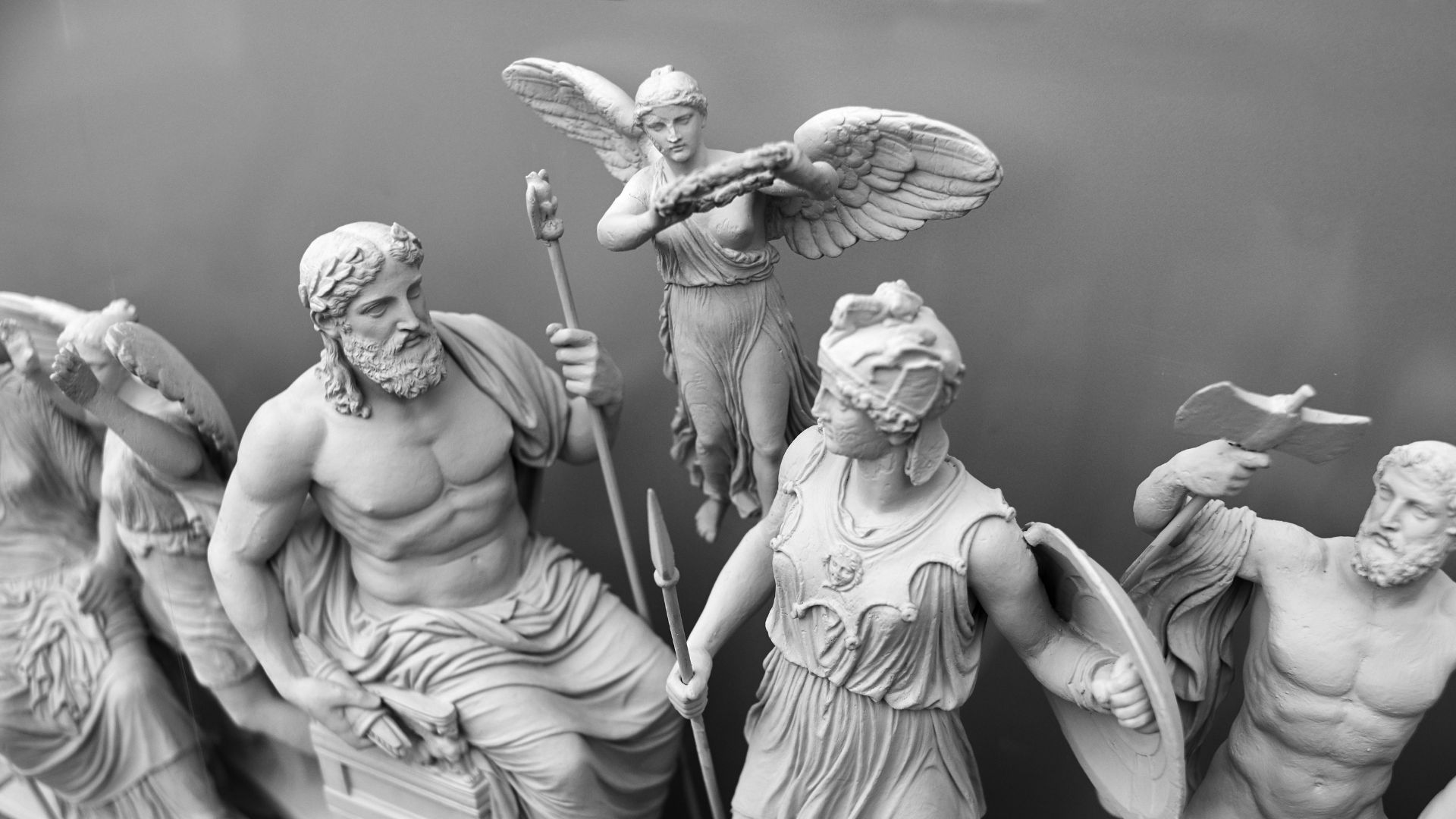 A stone statue of the philosopher Socrates is depicted sitting in a thoughtful pose, with his hand resting on his chin, against a clear blue sky.