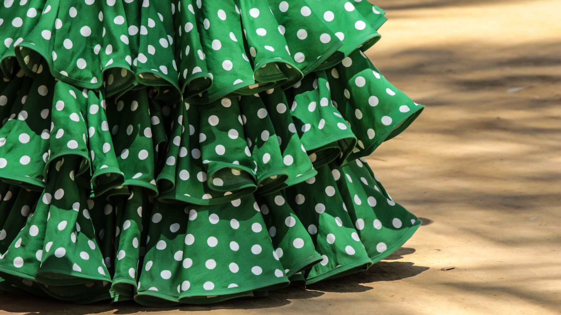 A close-up of the ruffled, layered skirt of a green flamenco dress with white polka dots.