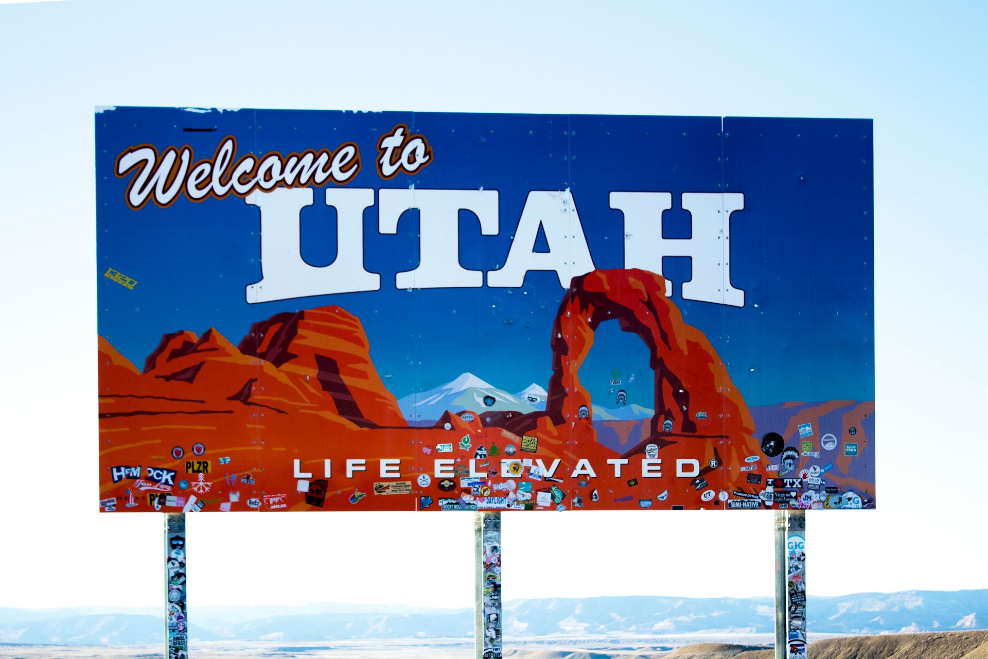 Welcome to Utah road sign with desert landscape and red rock formations in the background.