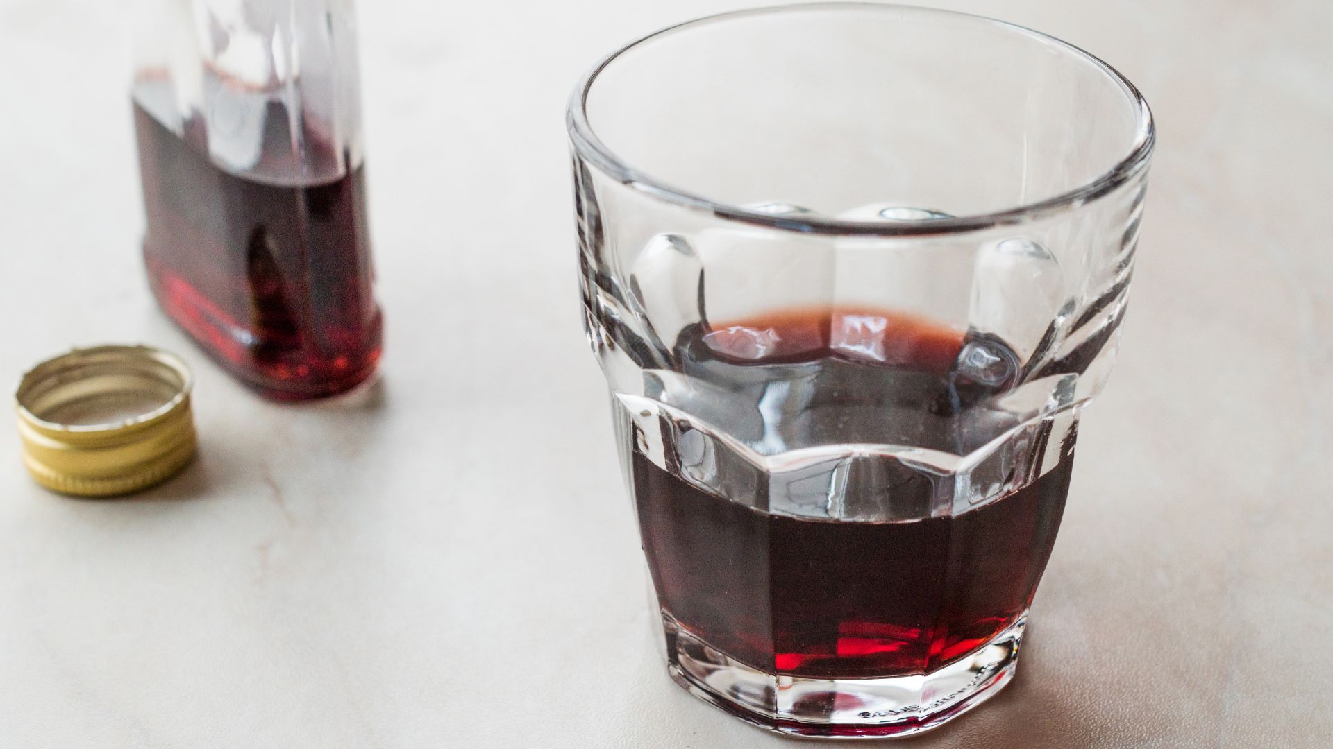 A close-up, overhead shot of a clear glass filled with a deep red liquid, likely cherry rakija or another red-hued fruit brandy.