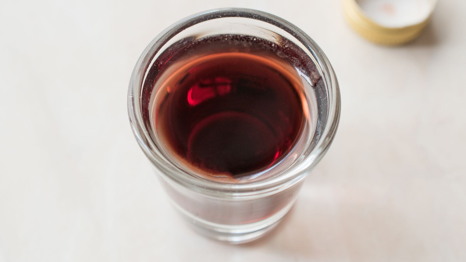 A close-up, overhead shot of a clear glass filled with a deep red liquid, likely cherry rakija or another red-hued fruit brandy.
