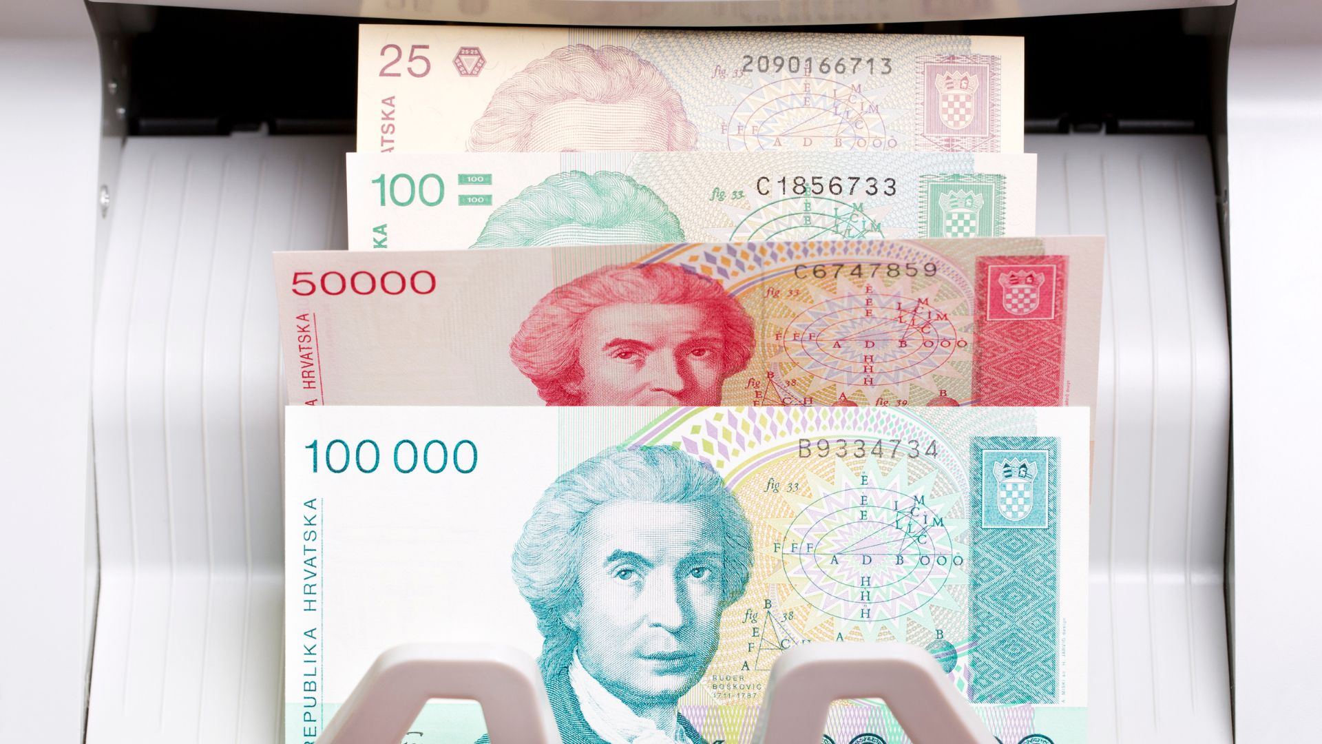 Croatian Dinar banknotes of various denominations (25, 100, 50,000, and 100,000) being fed into a money counting machine.