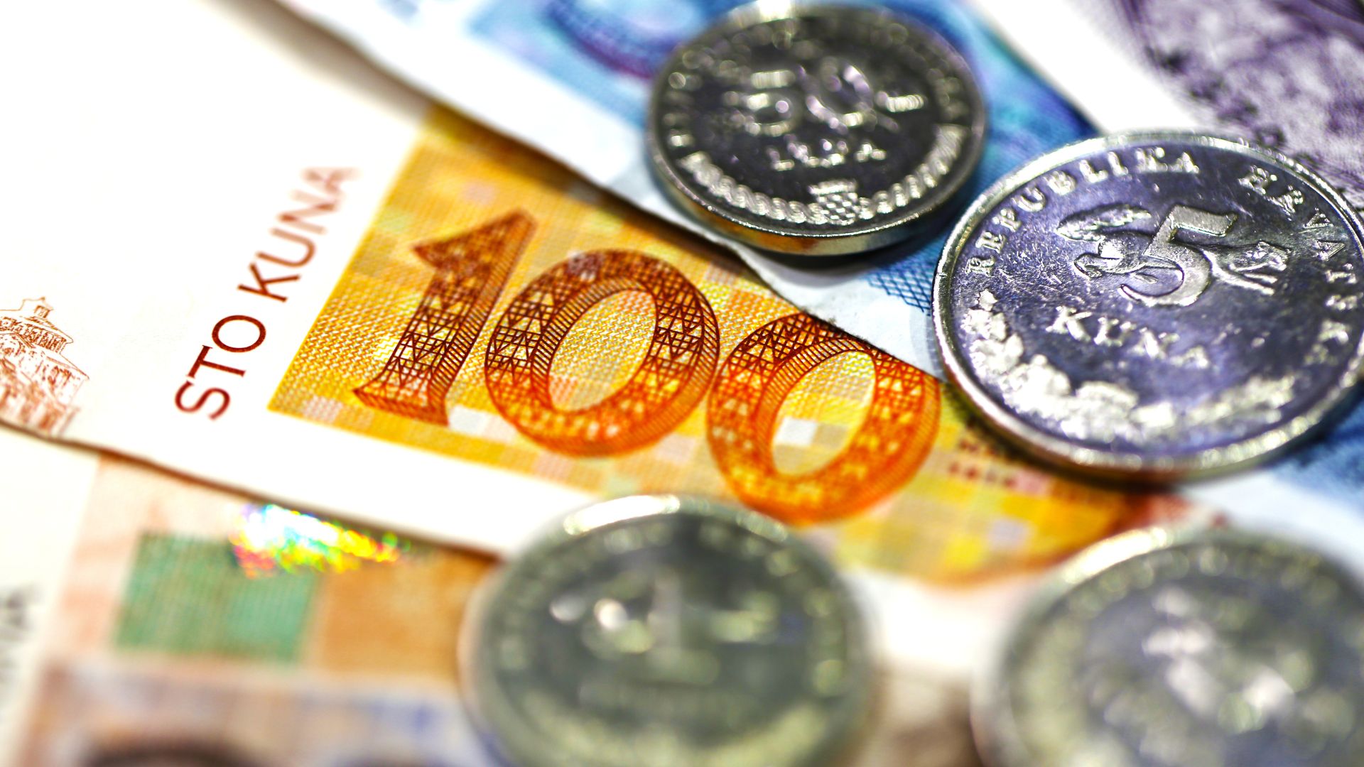 A close-up shot of Croatian Kuna banknotes and coins, including a 100 Kuna banknote and 5 Kuna coins, arranged on a surface.