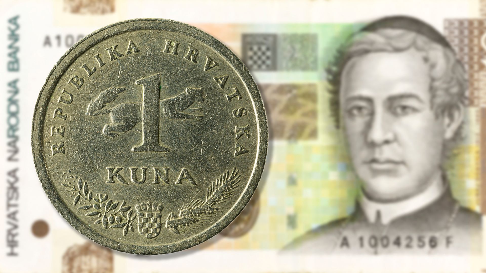 A Croatian 1 Kuna coin placed on top of a Croatian banknote featuring a portrait of Juraj Dobrila.