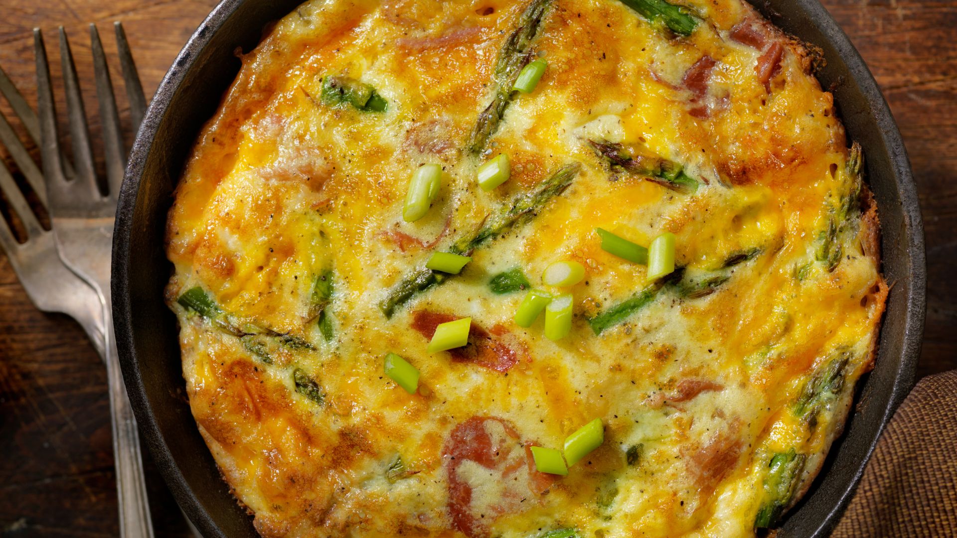 The image shows a baked egg dish with visible ingredients like asparagus and possibly ham or bacon, which are common additions to frittatas. 