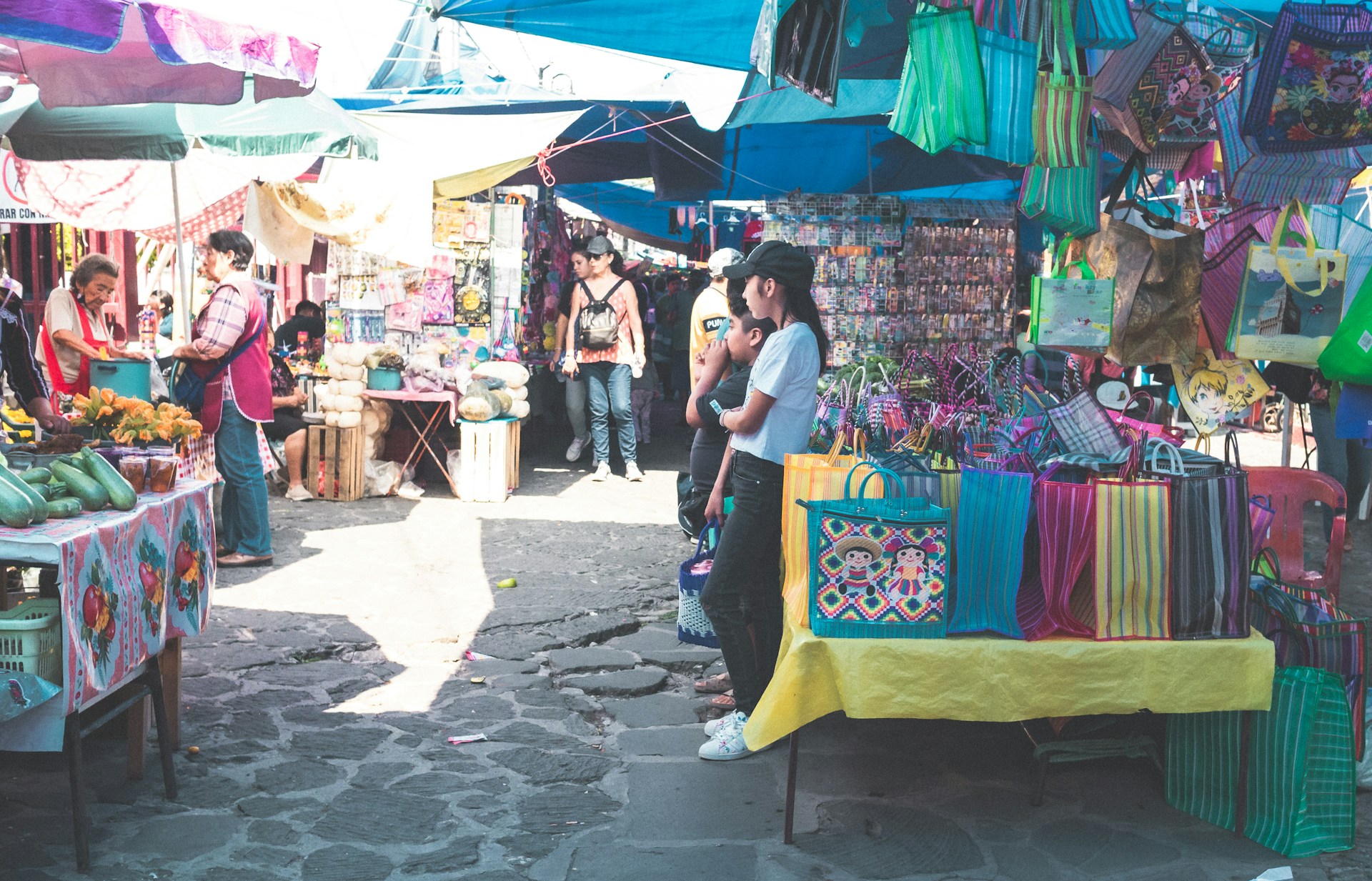 A vibrant Mexican street market with locals browsing through stalls of spices, fruits, and artisan goods.