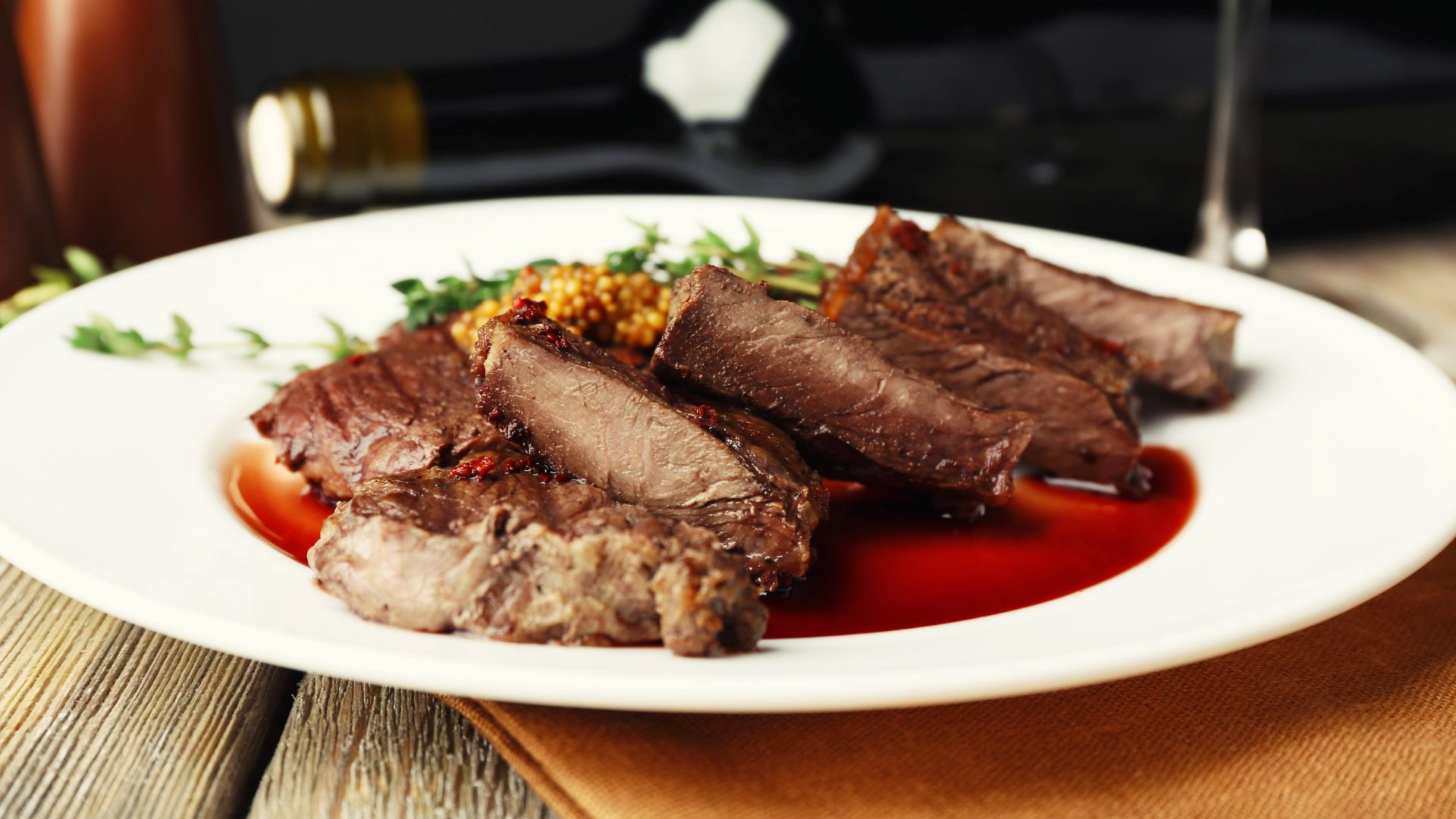 Yes, the image depicts cuts of meat, likely steak, served in a wine-based sauce. The presence of a rich, reddish sauce accompanying the meat, along with a bottle of wine in the background, strongly suggests a wine reduction or similar wine-based sauce. 
