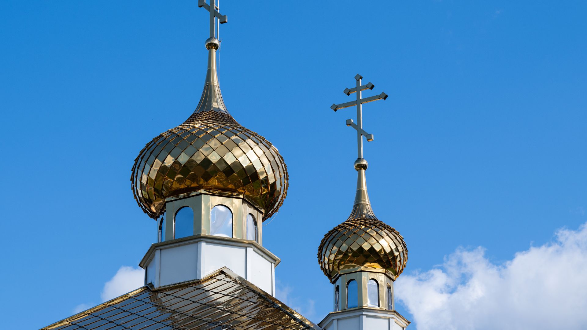 Close-up of two golden onion domes with Orthodox crosses on top, set against a clear blue sky with a few white clouds.