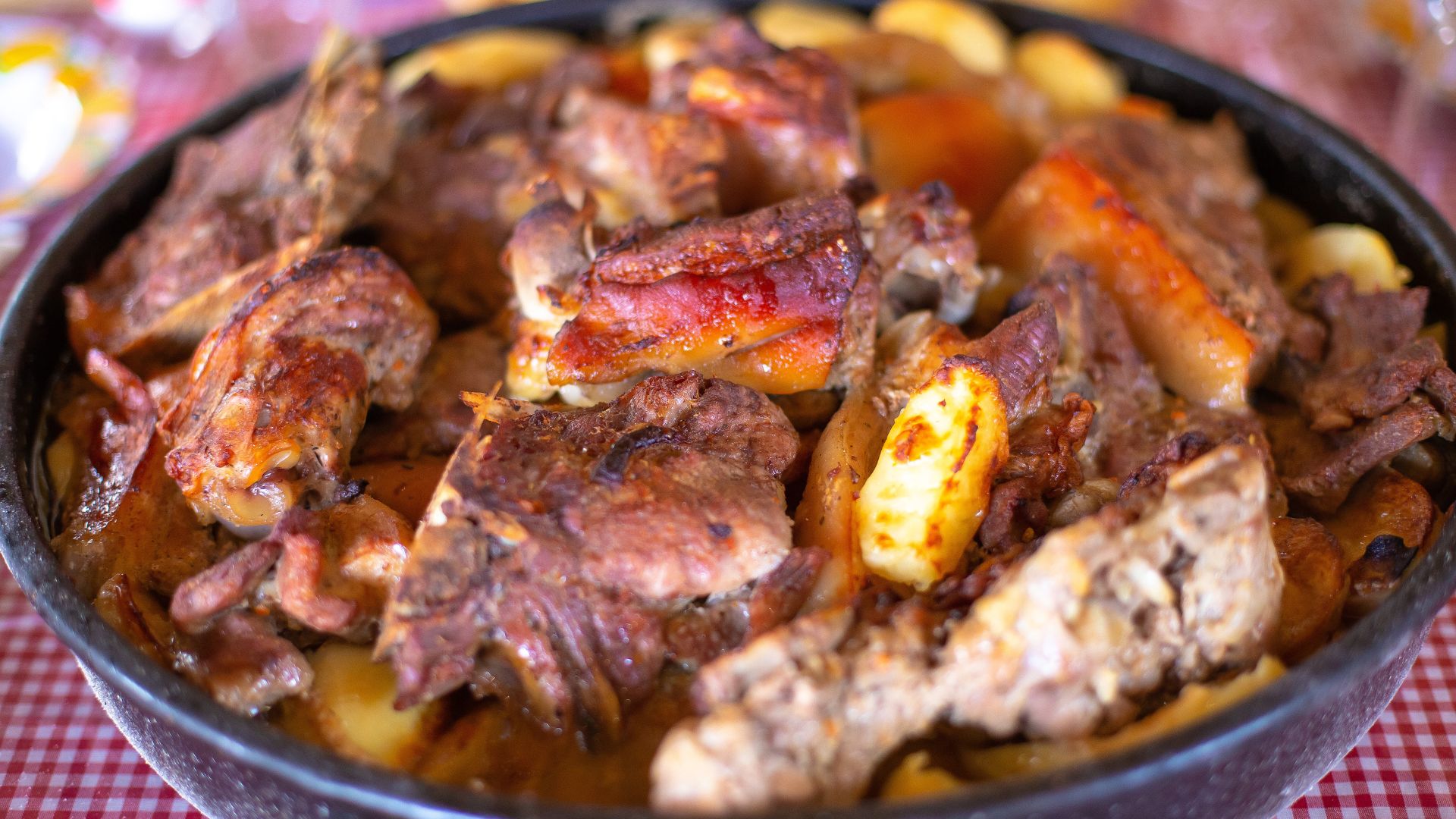 A close-up of a traditional Croatian "Peka" dish, featuring roasted meat (likely lamb or veal) and potatoes cooked under a bell-shaped lid, presented in a round cooking vessel. 