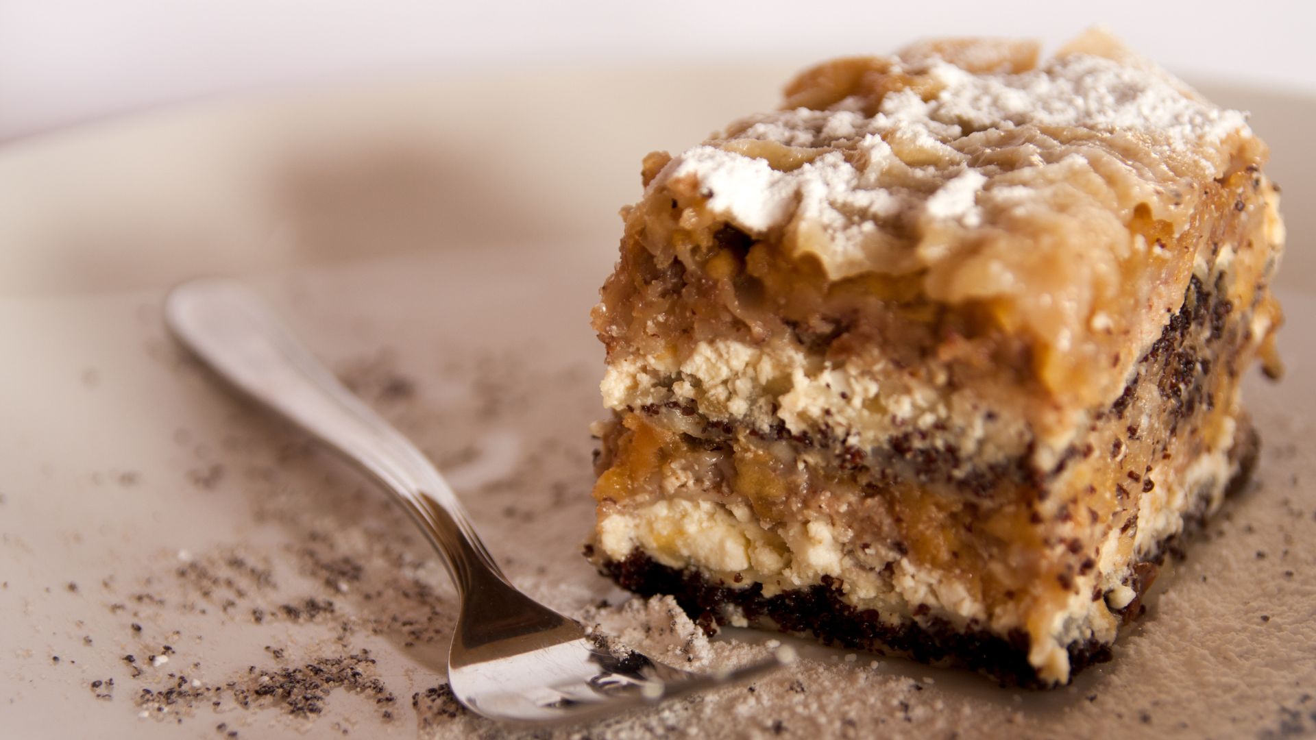 A close-up shot of a slice of layered Prekmurska Gibanica cake, topped with powdered sugar, and a fork resting beside it.