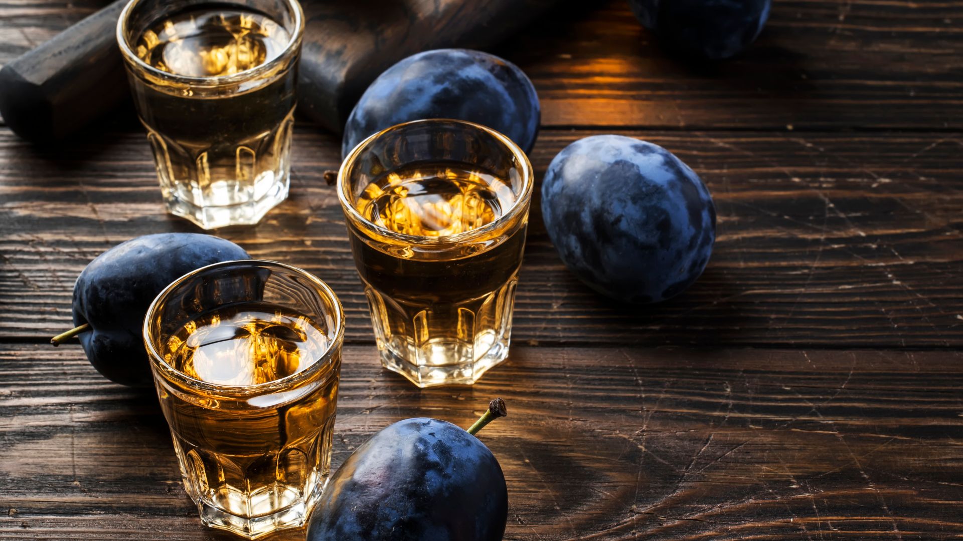 Glasses of plum brandy (Slivovica) on a rustic wooden table, accompanied by fresh plums.