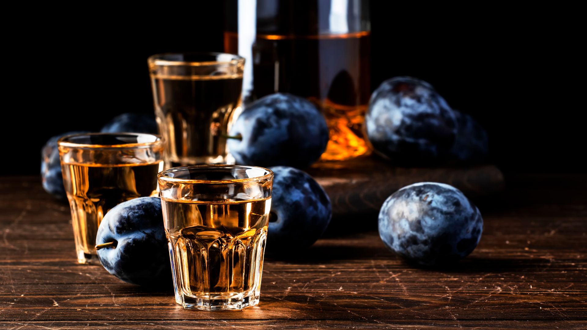 Glasses of plum brandy (Slivovica) on a rustic wooden table, accompanied by fresh plums.