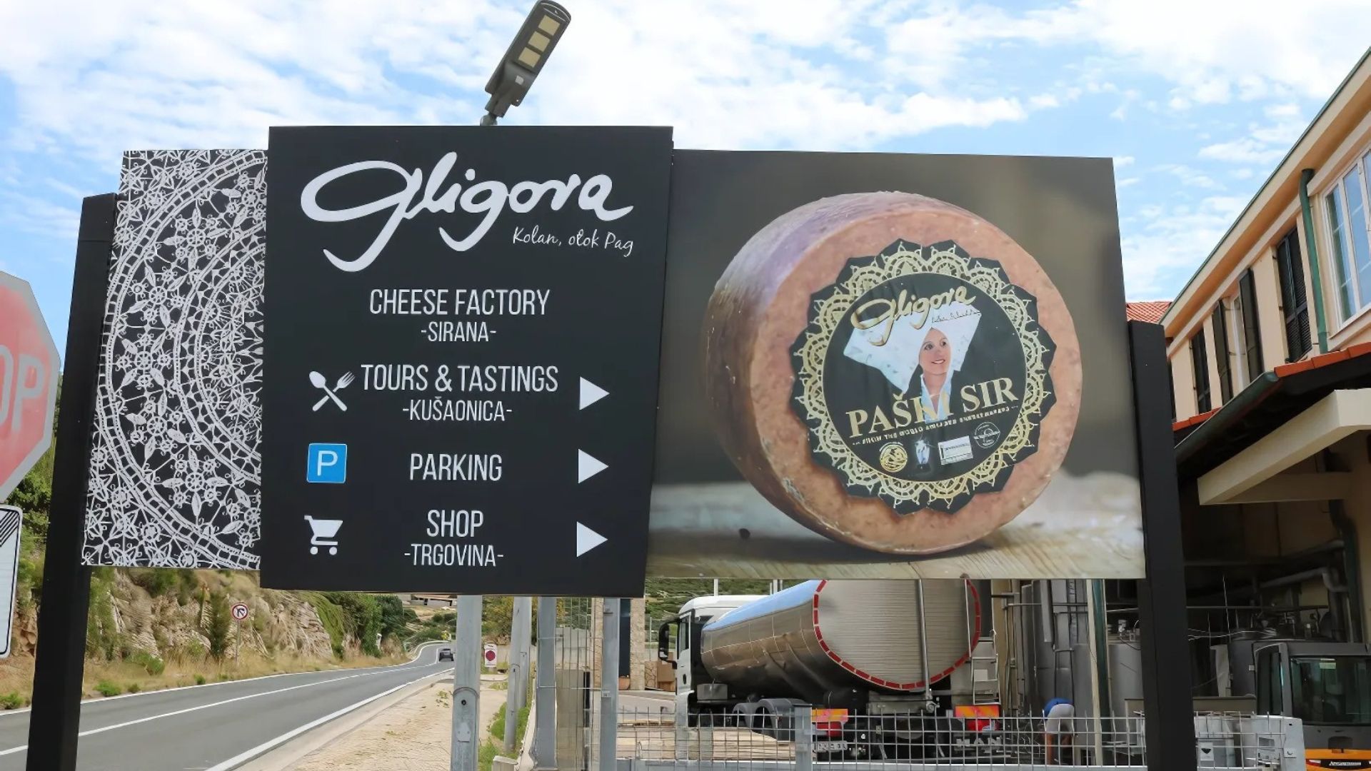  A roadside sign for the Gligora Cheese Factory on the island of Pag, Croatia, featuring information about tours, parking, and shop, alongside a large image of their renowned Paški sir cheese. 