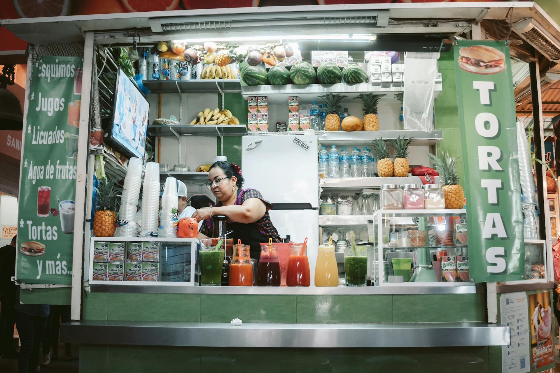 Mexican street vendor standing behind a small cart selling traditional food and drinks