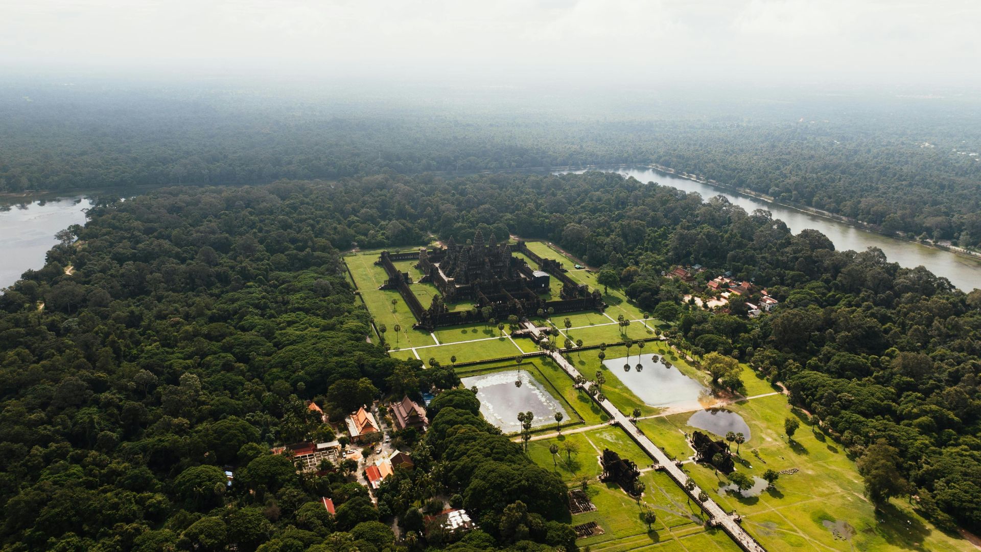 Stunning aerial footage of the Angkor Wat temple complex surrounded by lush forest and water reservoirs.