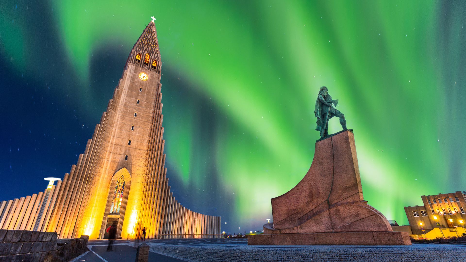 Hallgrímskirkja church and Leifur Eiríksson statue at night under the northern lights.
