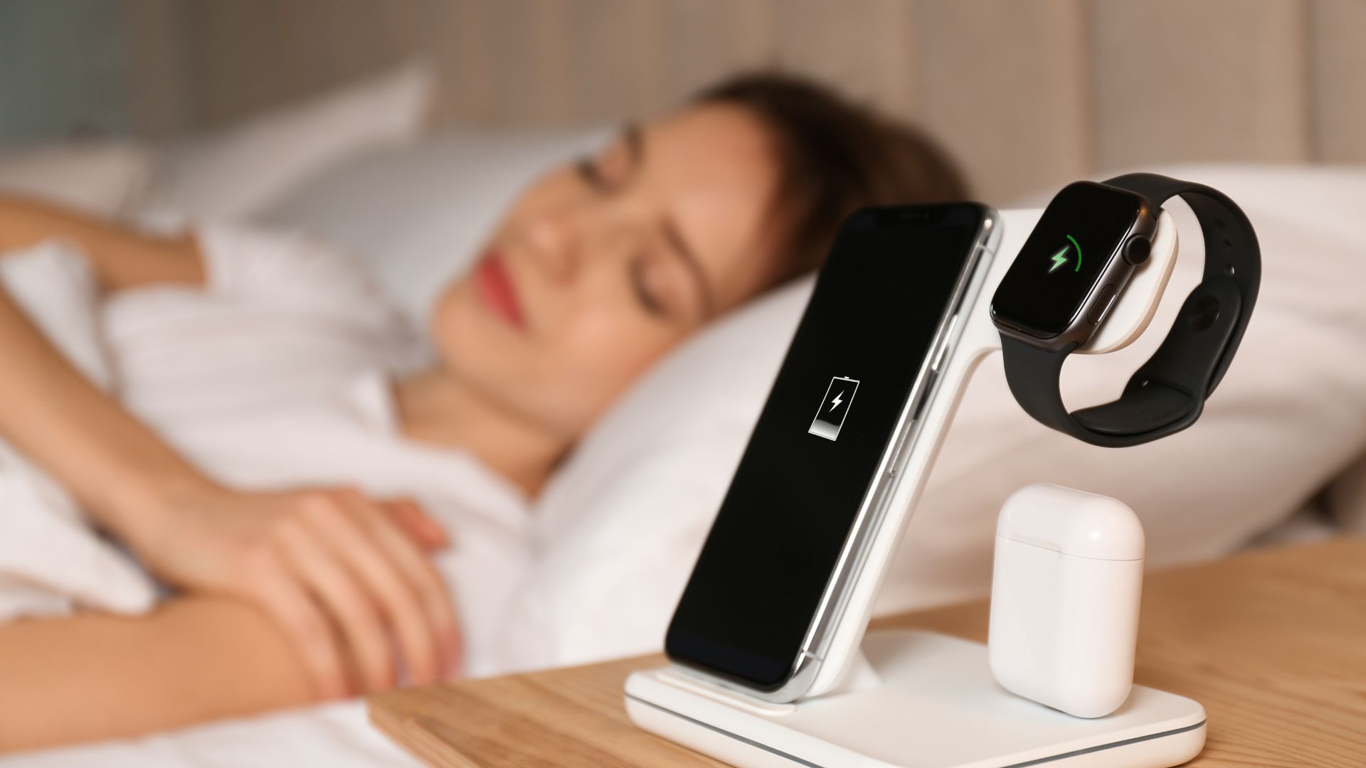 A woman sleeping with a phoe, watch, earphones on the bedside tabel