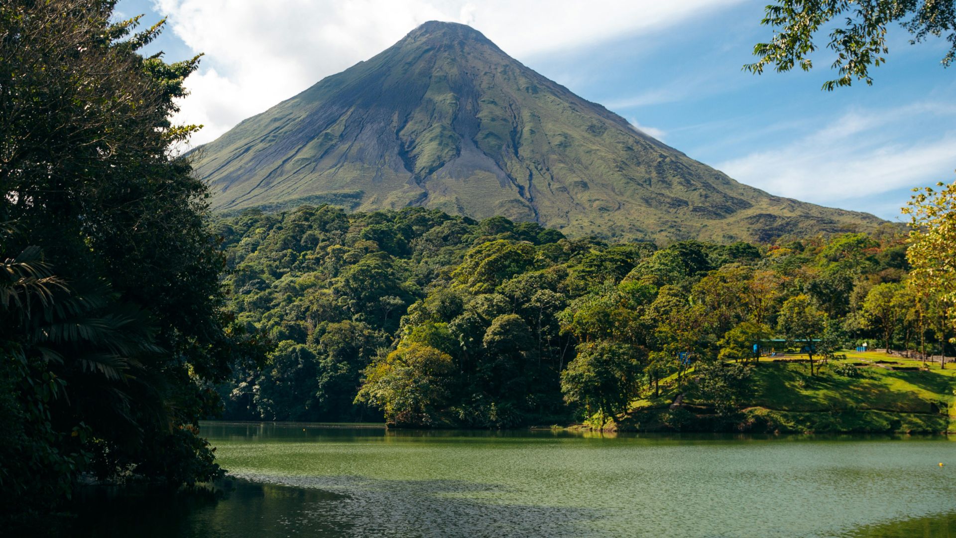 A view of the symmetrical Arenal Volcano rising above a lush green forest and reflecting in a lake