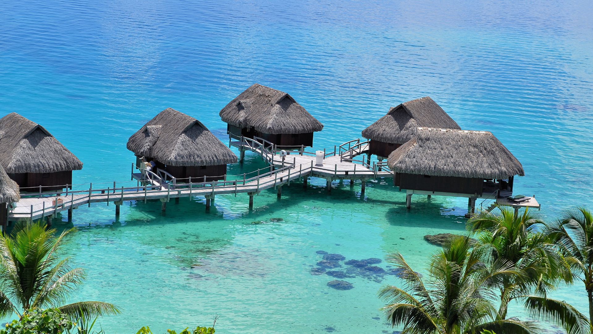 Scenic view of overwater bungalows with thatched roofs connected by wooden walkways over a clear turquoise lagoon in Bora Bora.