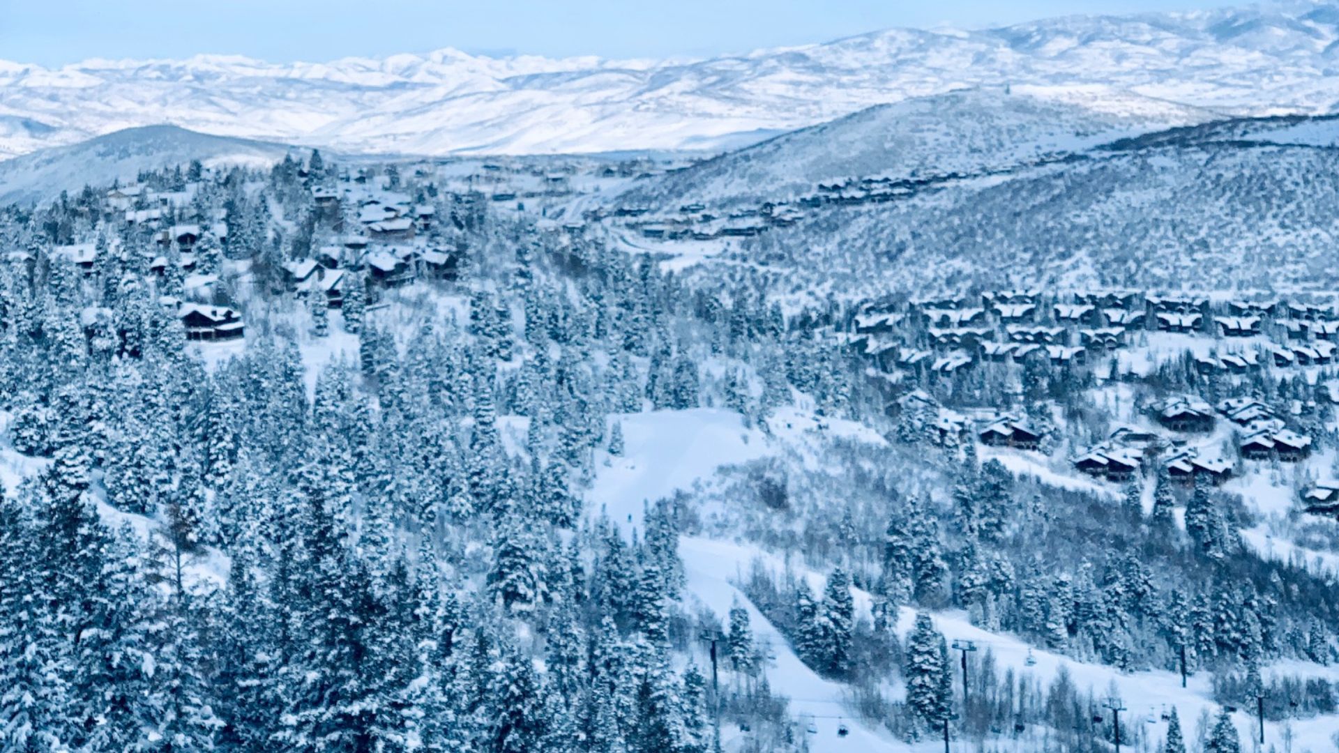 An aerial view of a snow-covered ski resort mountain with numerous luxury homes nestled among evergreen trees and ski runs.