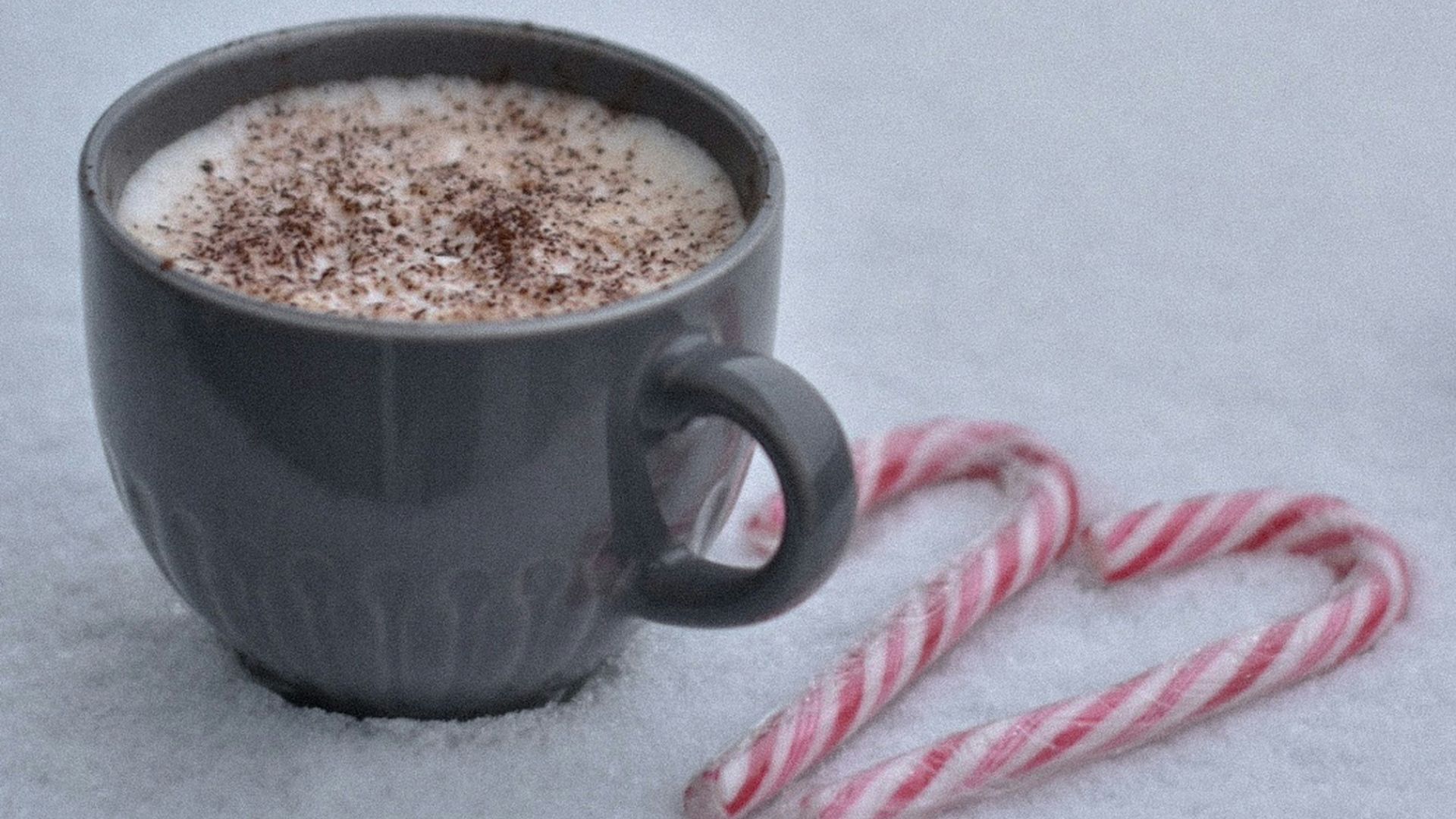 A cup of hot chocolate on snow with canady cranes.