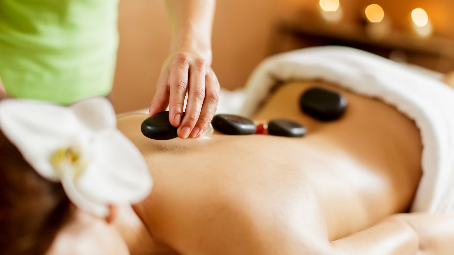 Image shows a therapist placing and moving several heated, smooth, dark stones along the recipient's back