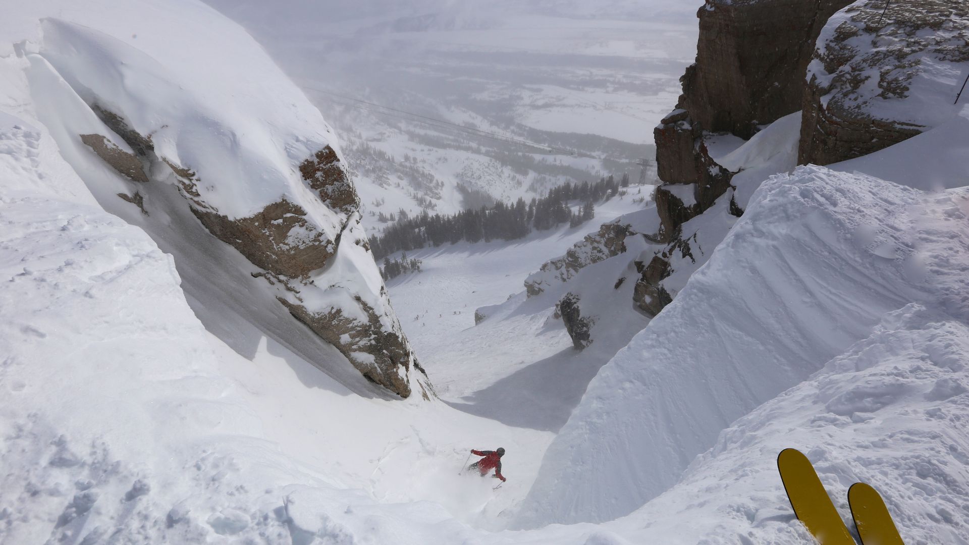 An expert skier in a red jacket drops into the steep, narrow, snow-covered Corbet's Couloir run between towering rock walls in Jackson Hole, Wyoming.