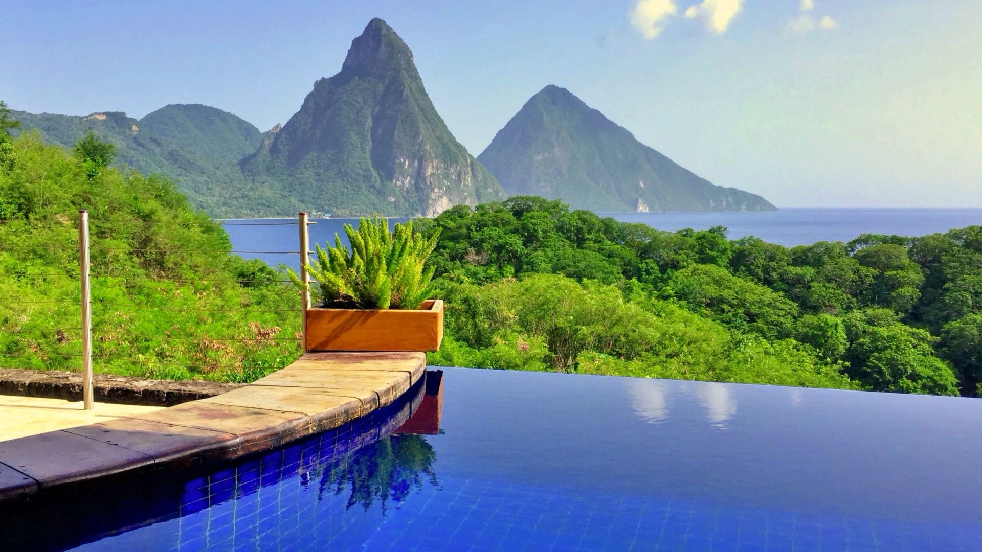 A serene infinity pool overlooks the majestic Pitons in St. Lucia. The lush greenery and clear skies create a breathtaking view.