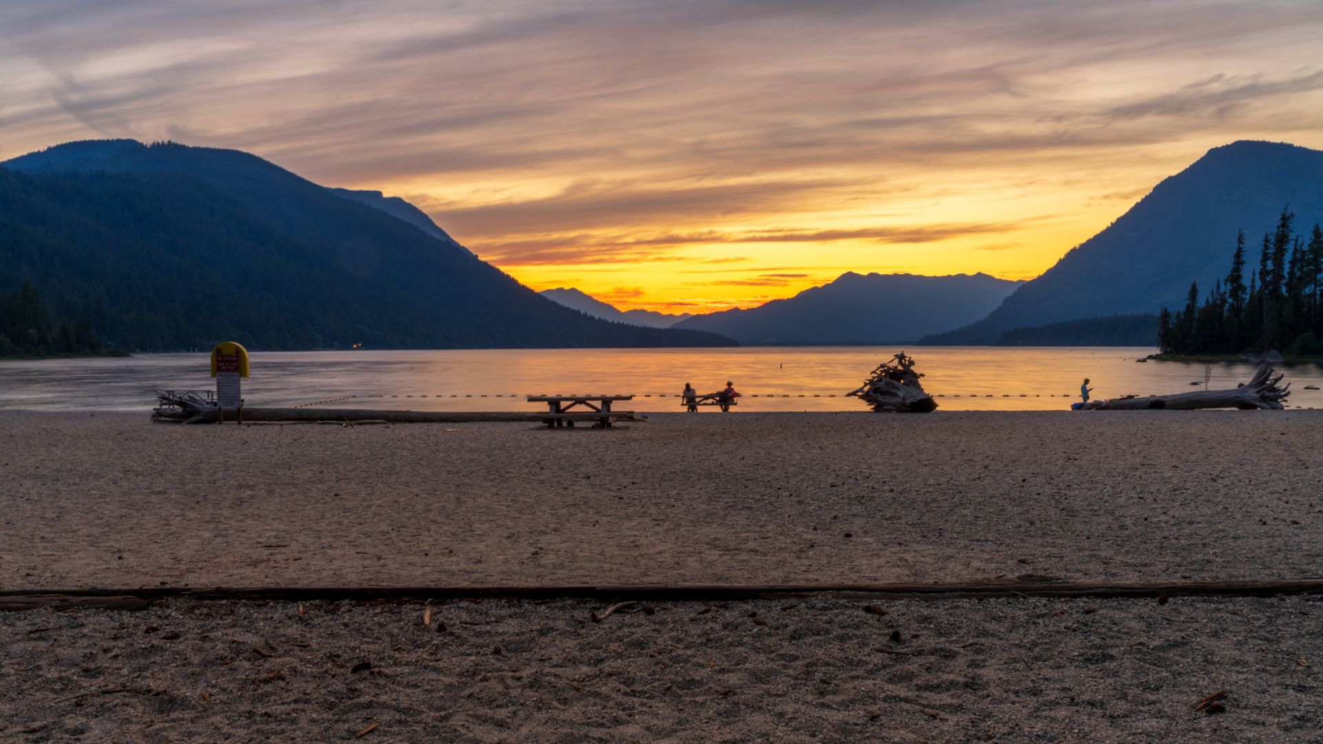 A sandy beach at Lake Wenatchee State Park with mountains in the background during a colorful sunset.