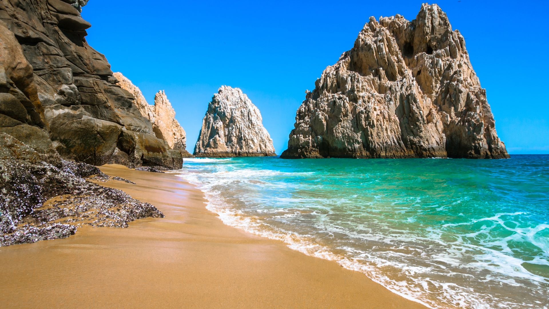 A stunning beach view of the rugged, pale granite cliffs and rock formations known as Land's End in Cabo San Lucas, Mexico.