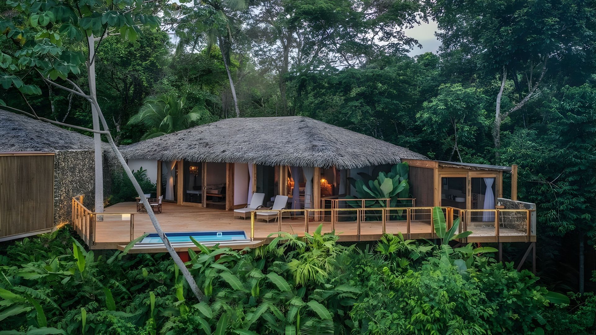 A thatched-roof jungle bungalow with a wooden deck and a small private pool, surrounded by dense tropical rainforest vegetation.