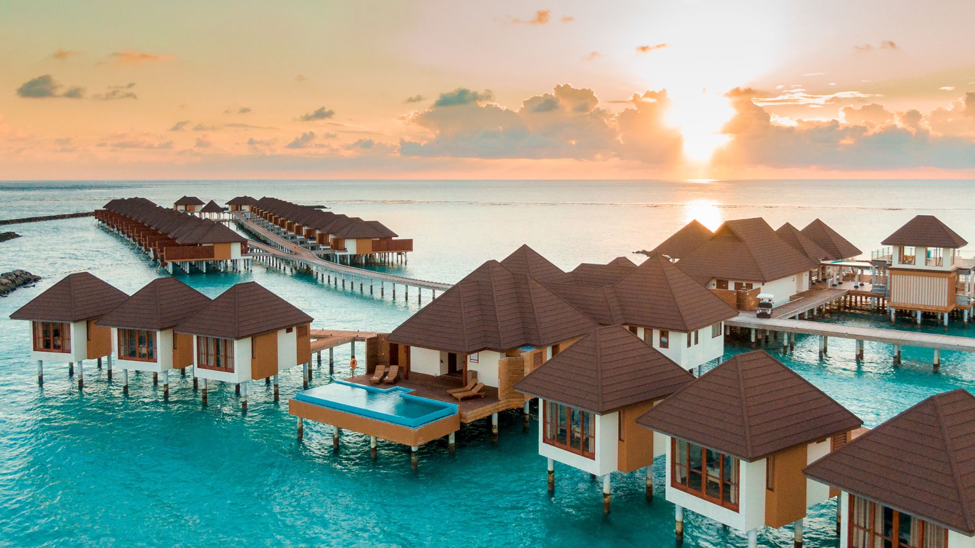 A tropical overwater bungalow resort in the Maldives at sunset.