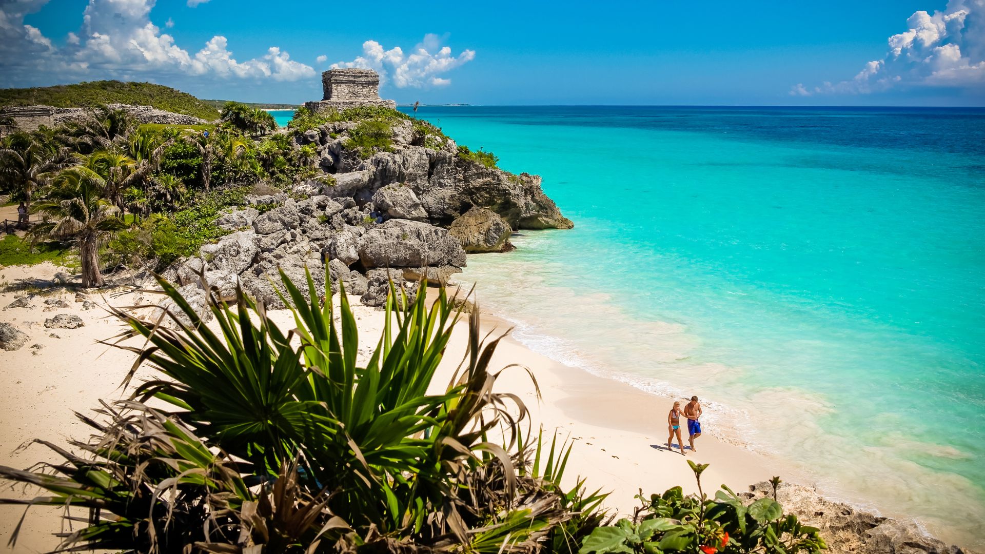 The ancient Mayan ruins of Tulum perched on cliffs overlooking a white sand beach and the turquoise Caribbean Sea.