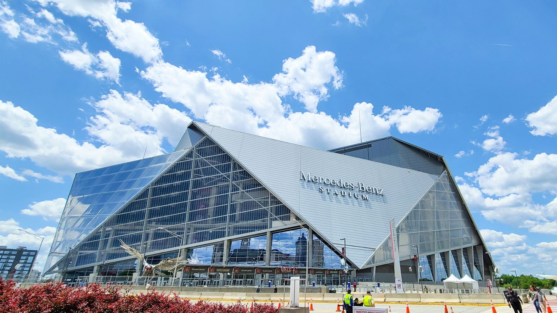 Exterior view of the modern, glass-and-metal Mercedes-Benz Stadium against a blue sky with white clouds.