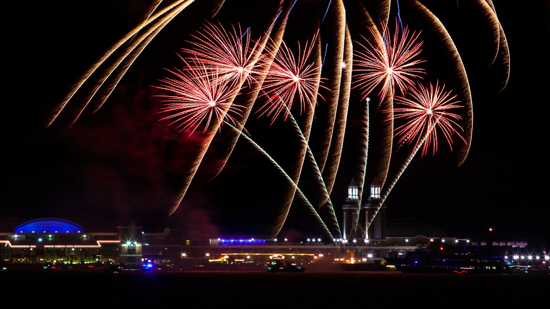 Colorful blue and gold fireworks exploding above the illuminated Navy Pier in Chicago at night.