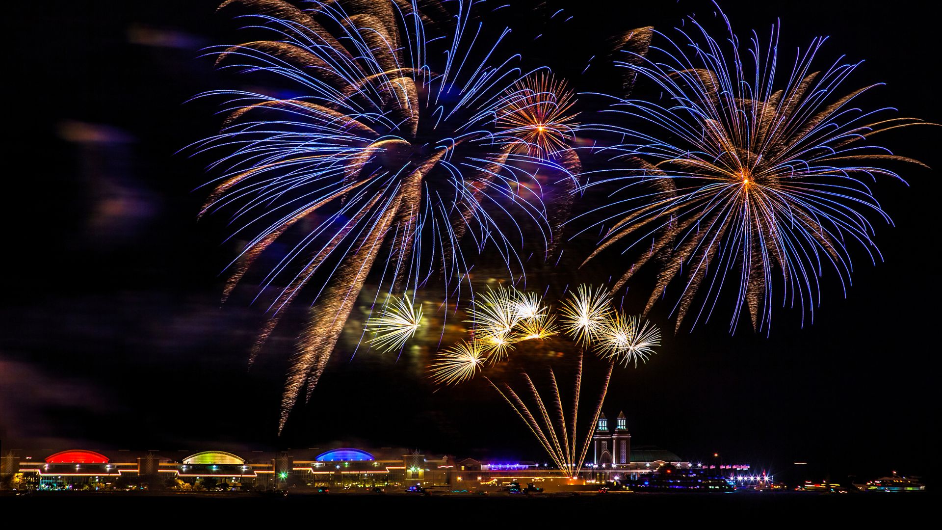 Colorful blue and gold fireworks exploding above the illuminated Navy Pier in Chicago at night.