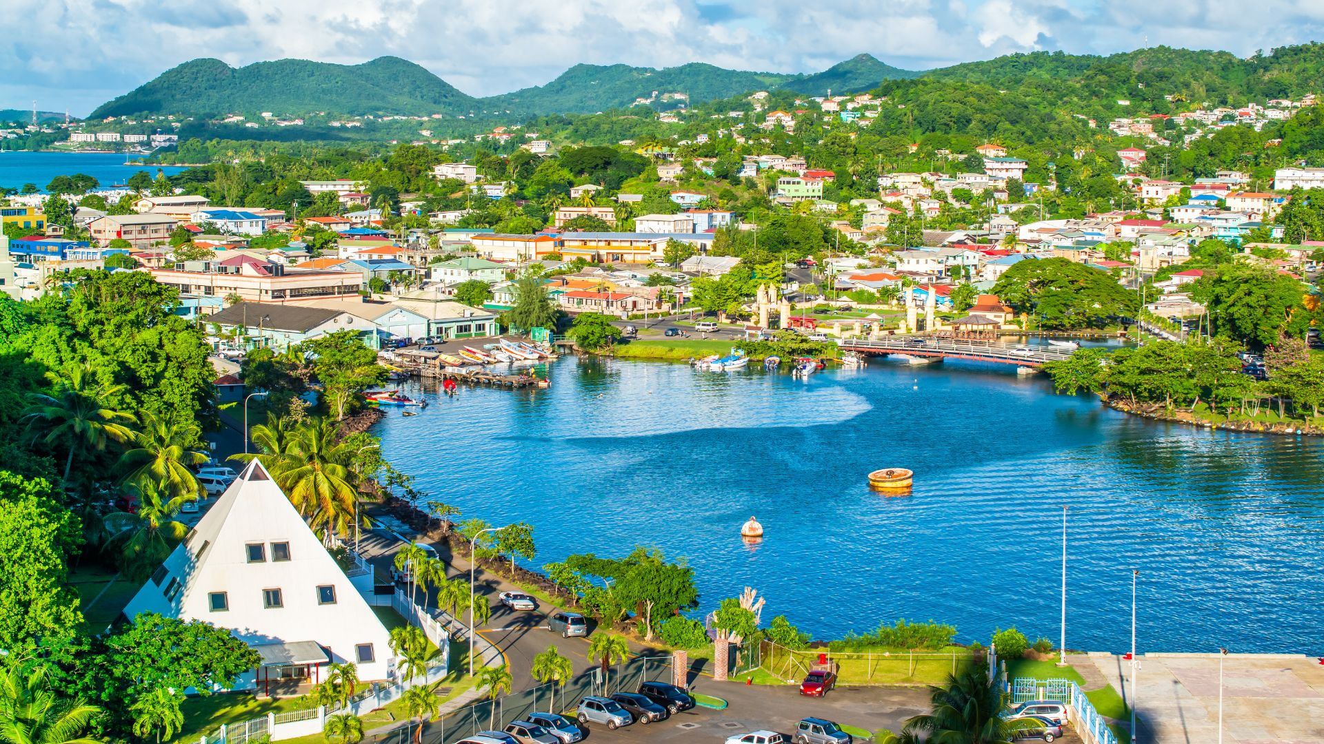 A high-angle view of the sheltered harbor and capital city of Castries, Saint Lucia, featuring colorful buildings along the waterfront and lush green hills in the background.