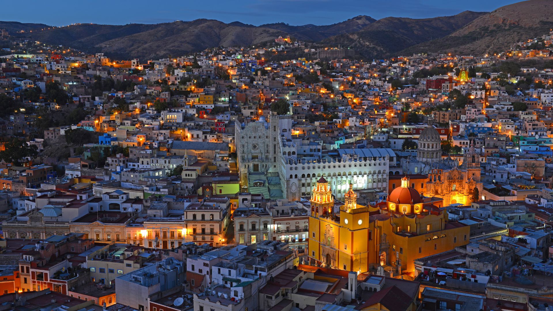 An aerial nighttime photo of the Santa Fe district in Mexico City, featuring several brightly lit modern skyscrapers and a large, illuminated urban park with winding pathways.