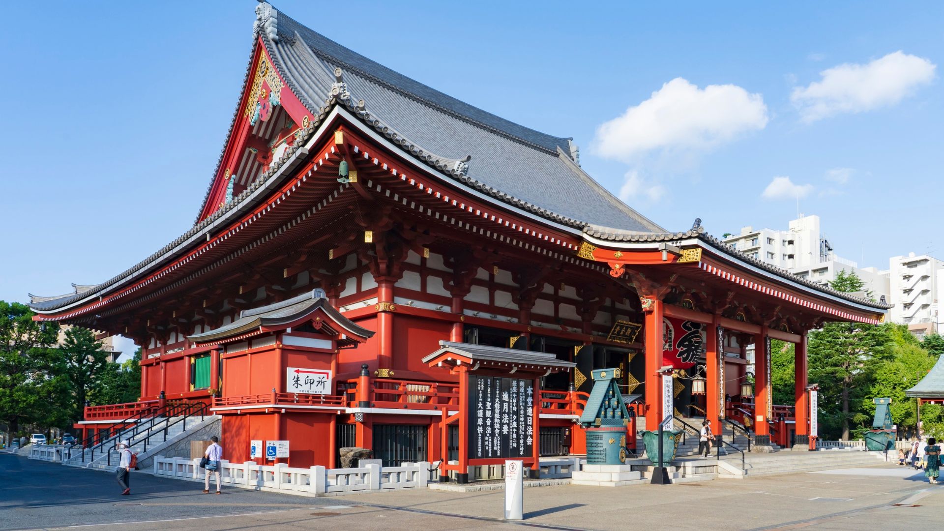 A large, traditional red Japanese temple building, the Sensō-ji, under a blue sky with some clouds.