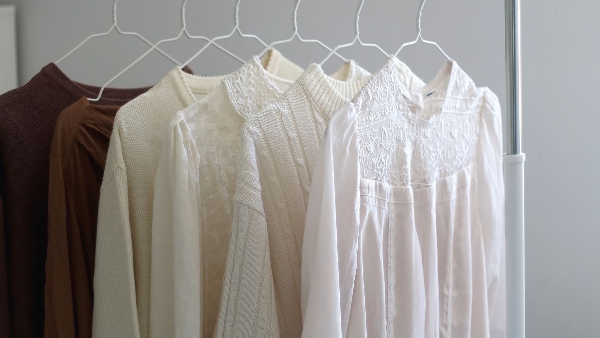 A minimalist, organized capsule wardrobe on a metal rack, featuring a variety of tops Wwith colors white. brown, and dark brown