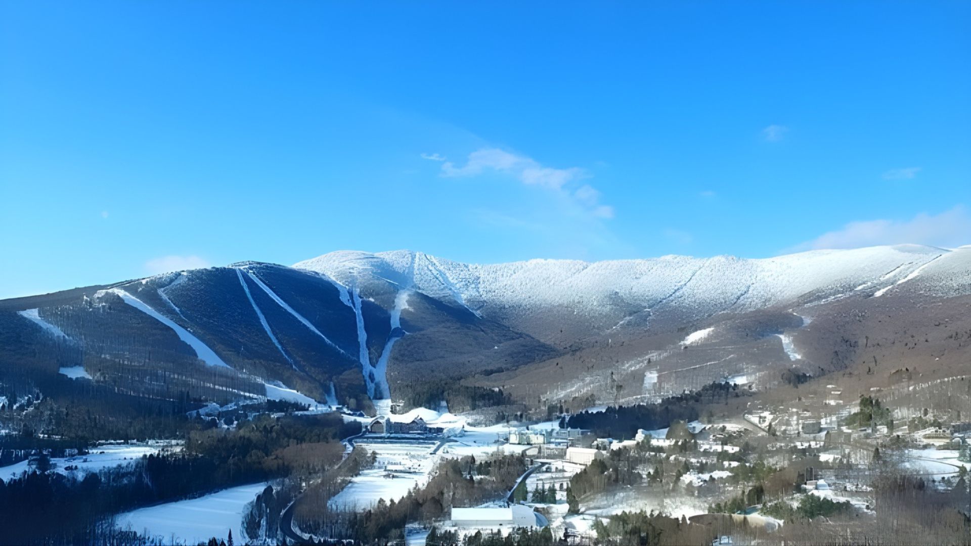 An aerial panoramic view of a snow-covered mountain ski resort in Vermont under a clear blue sky.