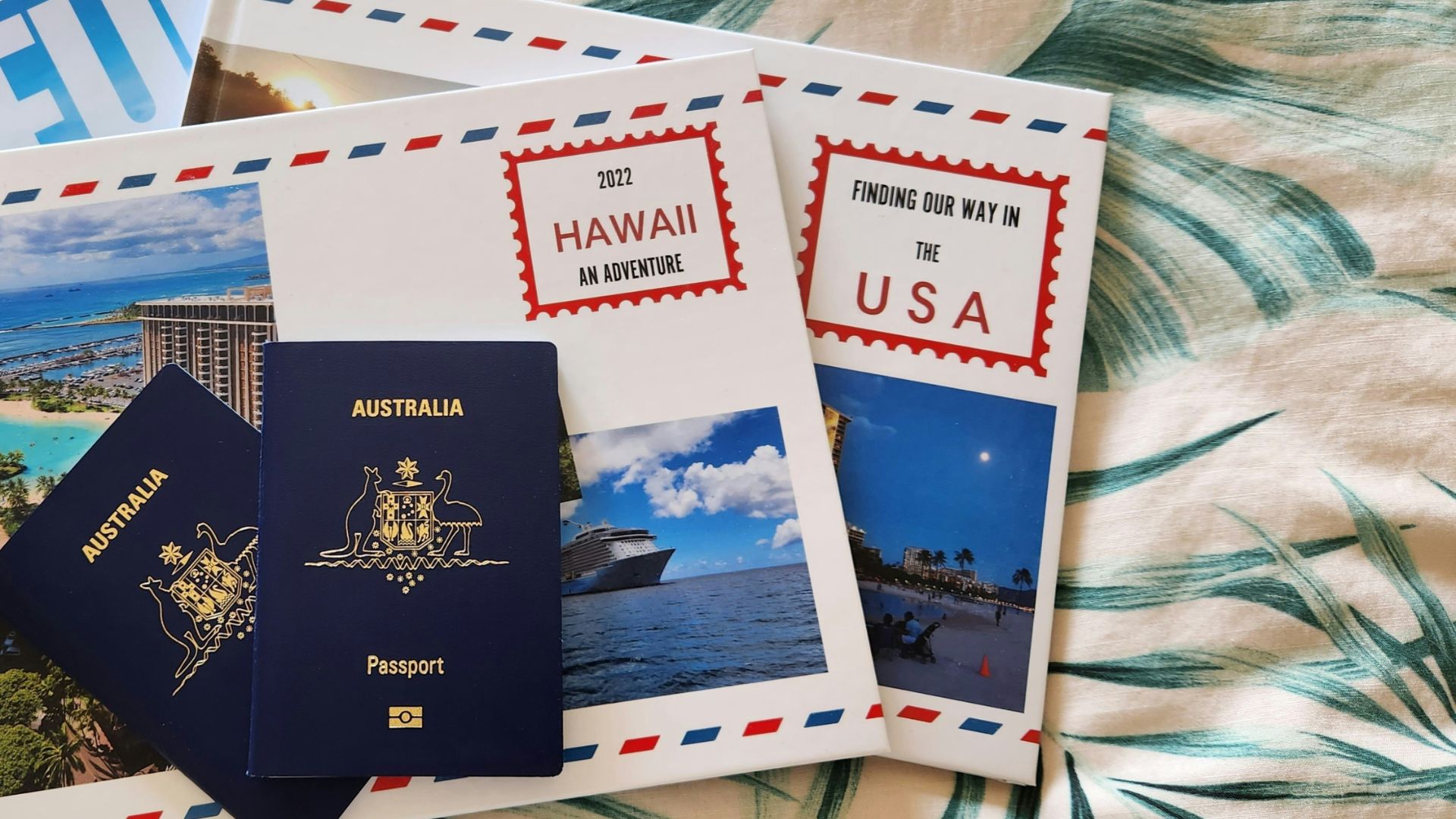 A flat lay of two Australian passports and several travel brochures for Hawaii and the USA on a tropical leaf-patterned background.
