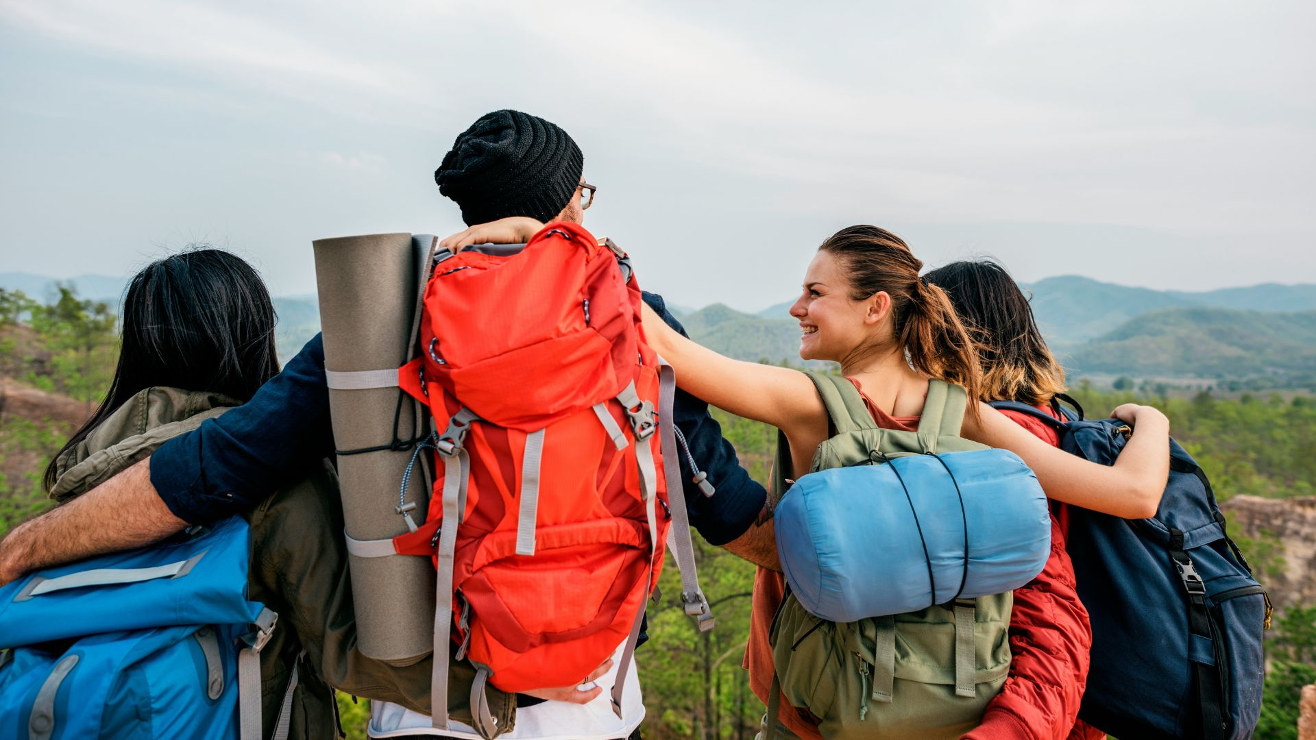 A group of four hikers with large backpacks views a mountainous landscape.