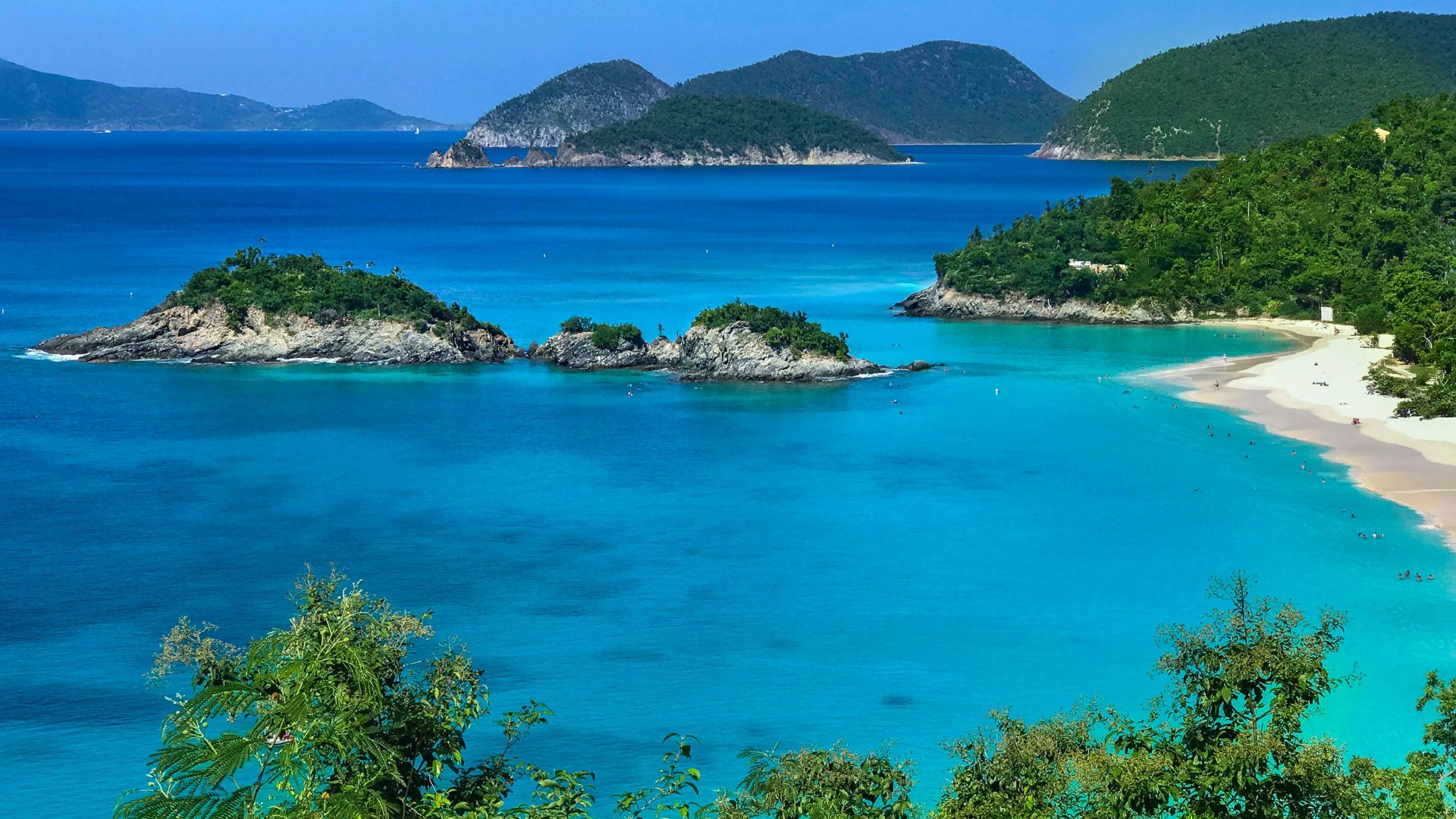 A stunning panoramic view of Trunk Bay on the island of St. John, U.S. Virgin Islands, featuring turquoise water, a white-sand beach, and small islands offshore.