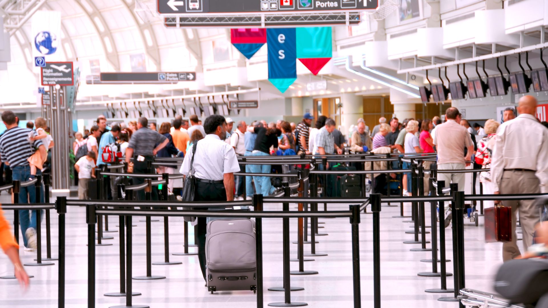 A photo of a busy airport customs hall with multiple queues of people and luggage waiting for processing.